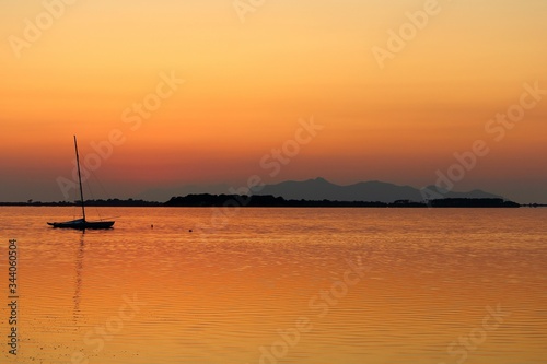 sailboat moored on the sea at sunset and headland on the background © massimo