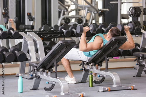 Sporty young man training with dumbbells in gym