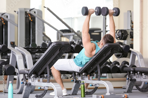 Sporty young man training with dumbbells in gym