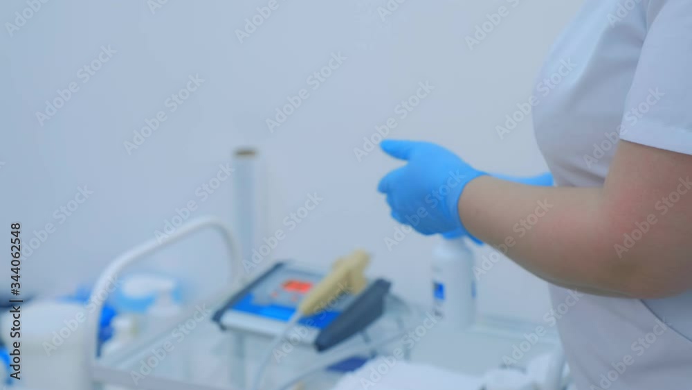 Doctor is spraying disinfectant on hands in gloves in clinic before procedure, closeup hands. Woman is preparing to therapy, treatment, cure in room of hospital. Medical worker disinfects hands. Doctor is spraying disinfectant on hands in gloves in clinic before procedure, closeup hands. Woman is preparing to therapy, treatment, cure in room of hospital. Medical worker disinfects hands.