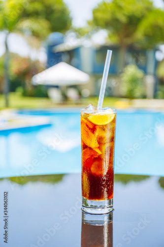 Photography Glass of cuba libre cocktail with lemon on the table closed to swimming pool