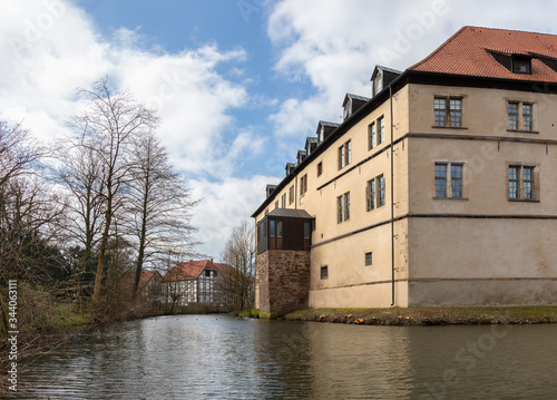 A moat in front of the historic Brake castle near the German city of Lemgo. It is winter with a blue sky and clouds. In the background a beautiful, old half-timbered house.