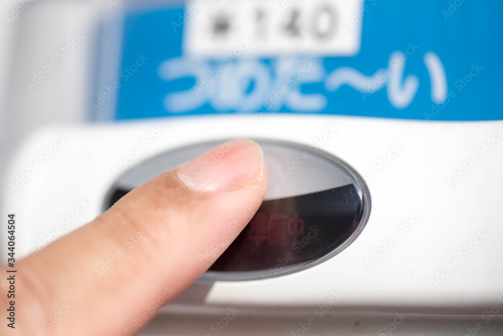 A finger pressing a button on a Japanese vending machine to buy a drink beverage which costs 140 yen. The Japanese character is read a tsumetai which means cold. A finger pressing a button on a Japanese vending machine to buy a drink beverage which costs 140 yen. The Japanese character is read a tsumetai which means cold.