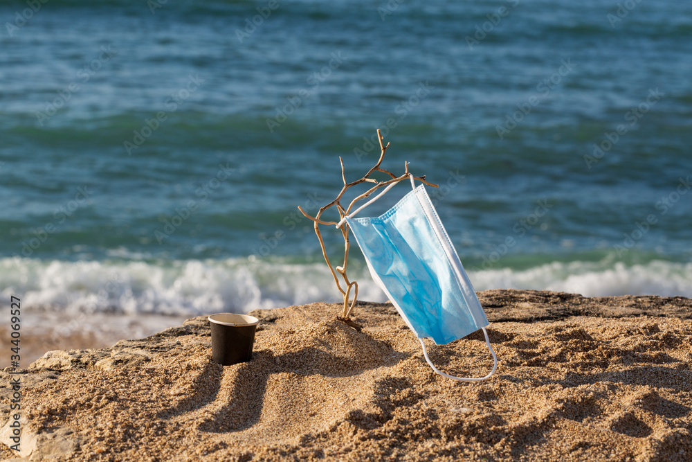 Medical protective mask is left abandoned on the beach. It must be disposed in a proper hazardous waste bin, preventing germs spread. Objects and medical supply waste management. Medical protective mask is left abandoned on the beach. It must be disposed in a proper hazardous waste bin, preventing germs spread. Objects and medical supply waste management.