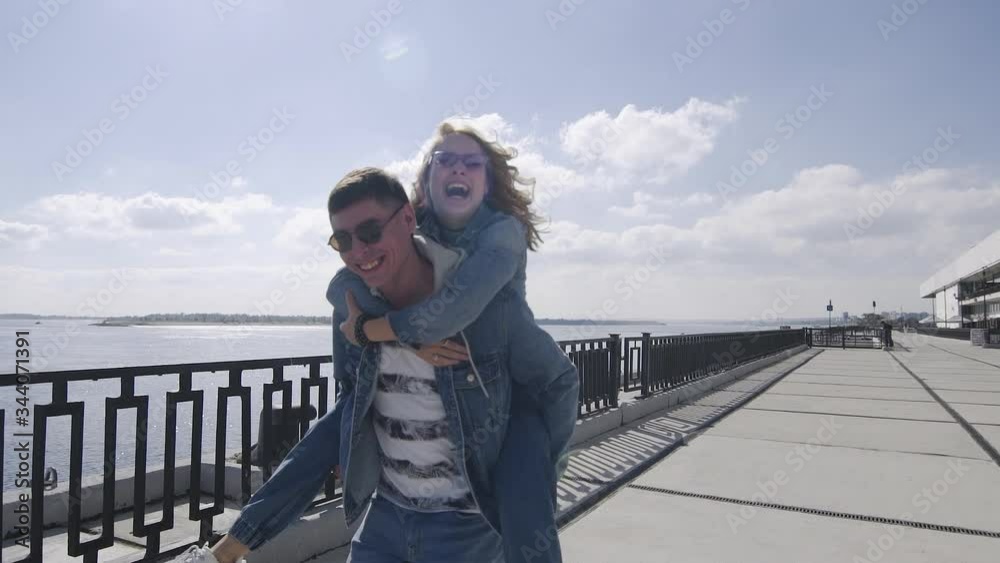 Young man carries on his back a woman and runs on promenade Young man carries on his back a woman and runs on promenade