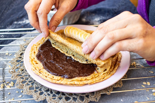 Crepes with chocolate and bananas or thin pancakes. Vegan food sweet breakfast. Woman hands