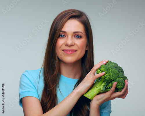 Smiling woman in blue dress holding big green broccoli.