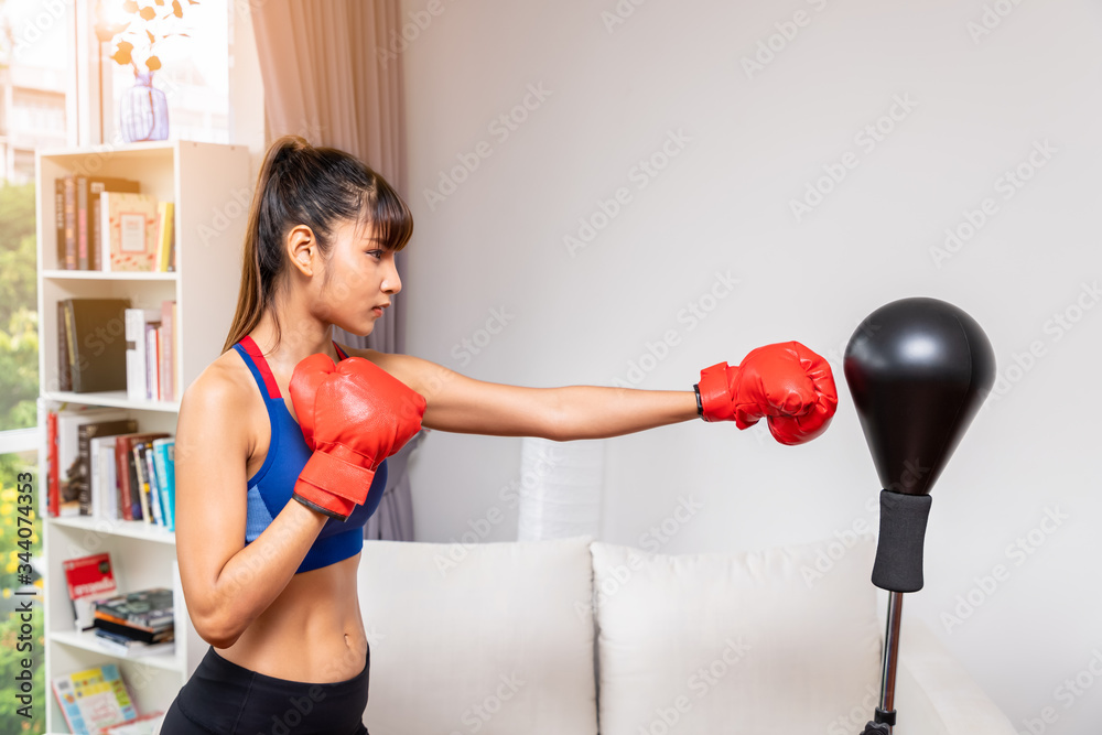 Φωτογραφία Female woman boxer hitting punching bag in living room at home, practice martial