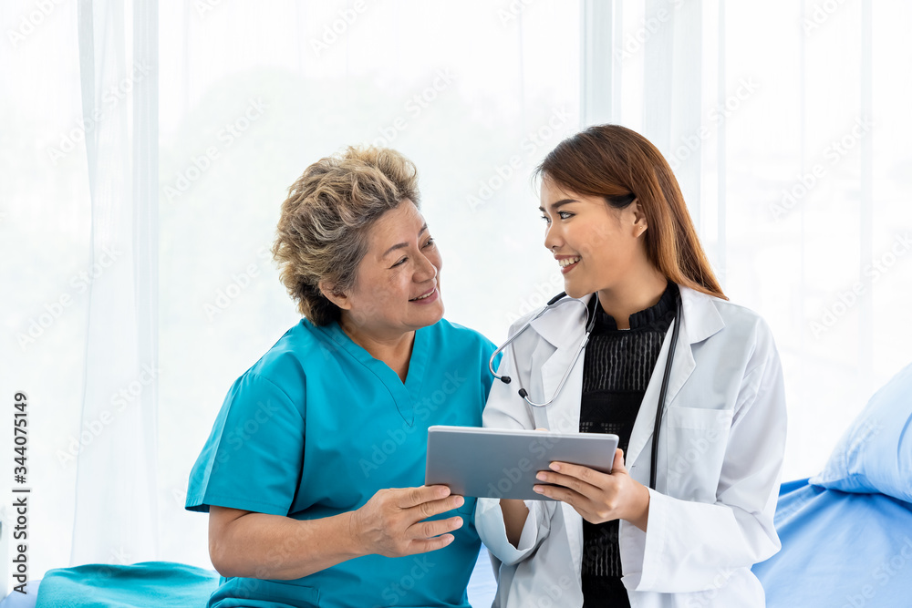 Asian medical doctor take care and explain senior elderly woman female patient sitting on bed with tablet Asian medical doctor take care and explain senior elderly woman female patient sitting on bed with tablet