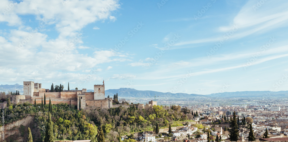 Panoramic view of the Alhambra in Granada with the city in the background a sunny day with blue sky and white clouds.