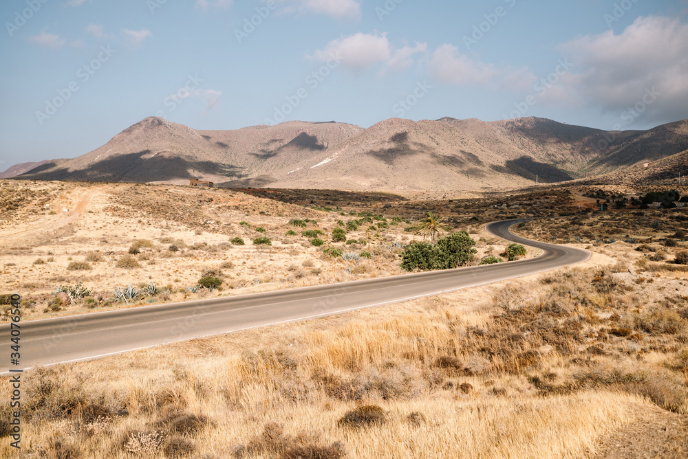 Winding road that is lost between desert mountains with blue sky and clouds.