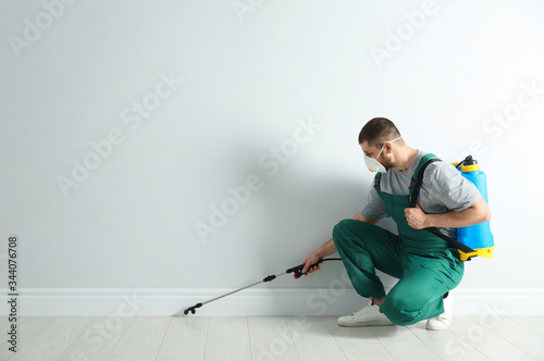 Pest control worker in uniform spraying pesticide indoors. Space for text photo