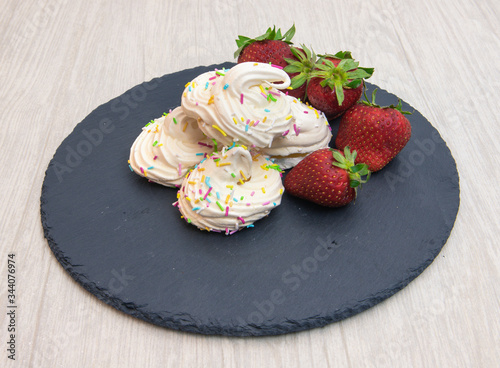 
meringues with strawberries on black plate and white background photo