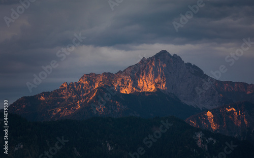 Sunlight in mountains during sunrise at lake Forggensee, dramatic dark clouds in the sky, Bavaria.