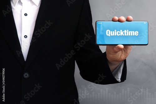 Quicktime. Businessman in a suit holds a smartphone at the camera. The term Quicktime is on the phone. Concept for business, finance, statistics, analysis, economy photo