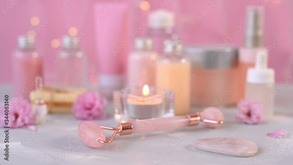 rose quartz roller lies among various bottles with beauty acids and burning candle in bathroom close view rose quartz roller lies among various bottles with beauty acids and burning candle in bathroom close view