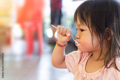 Soft focus    of    Happy Asian baby child girl   eating yogurt food by herself. Her face is sloppy and messy. 2-3    years    old    baby.    Kid and food concept.