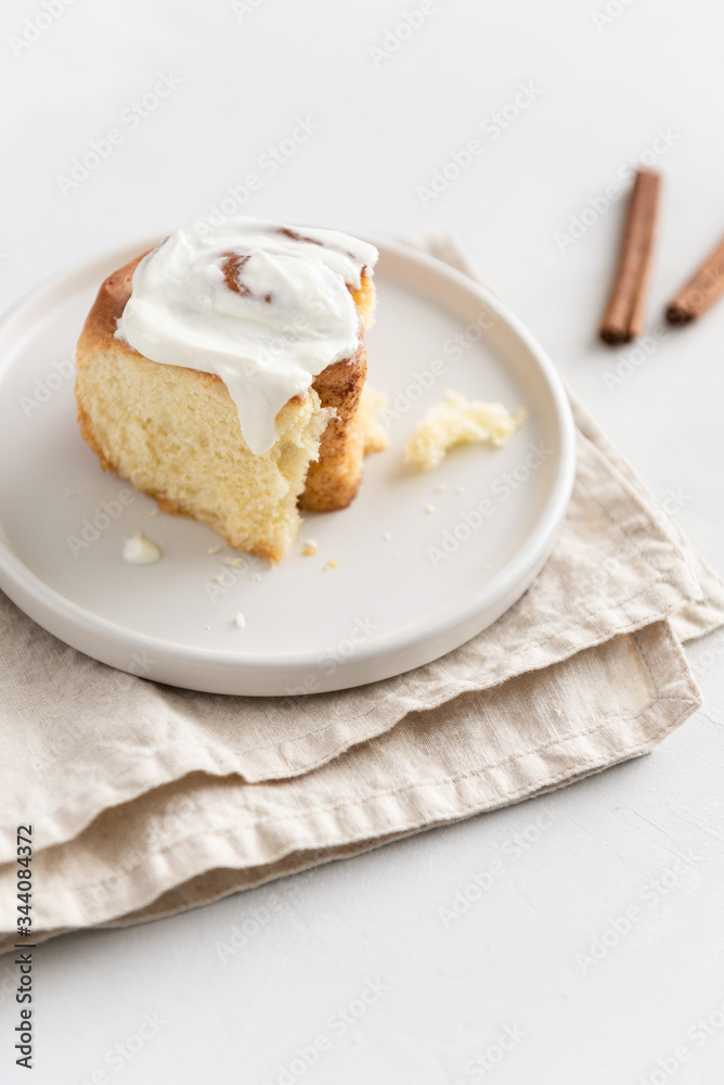 Cinnamon roll or cinnabon with white cream glaze on gray plate on white background. Cinnabons recipe. Traditional homemade sweet buns. Pastry, bakery. Side view Cinnamon roll or cinnabon with white cream glaze on gray plate on white background. Cinnabons recipe. Traditional homemade sweet buns. Pastry, bakery. Side view