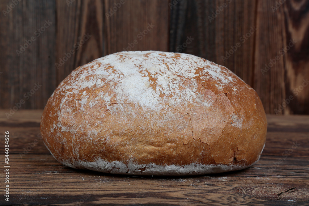 Side view of a fresh, crunchy, round bread sprinkled with flour on a rusted wooden table with brown boards. Side view of a fresh, crunchy, round bread sprinkled with flour on a rusted wooden table with brown boards.