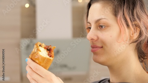 Portrait of smiling woman with dirty ketchup face  greedily eagerly eating food during quarantine due to coronavirus. Charming happy hungry woman laugh and holds in hands big meat pie. 
