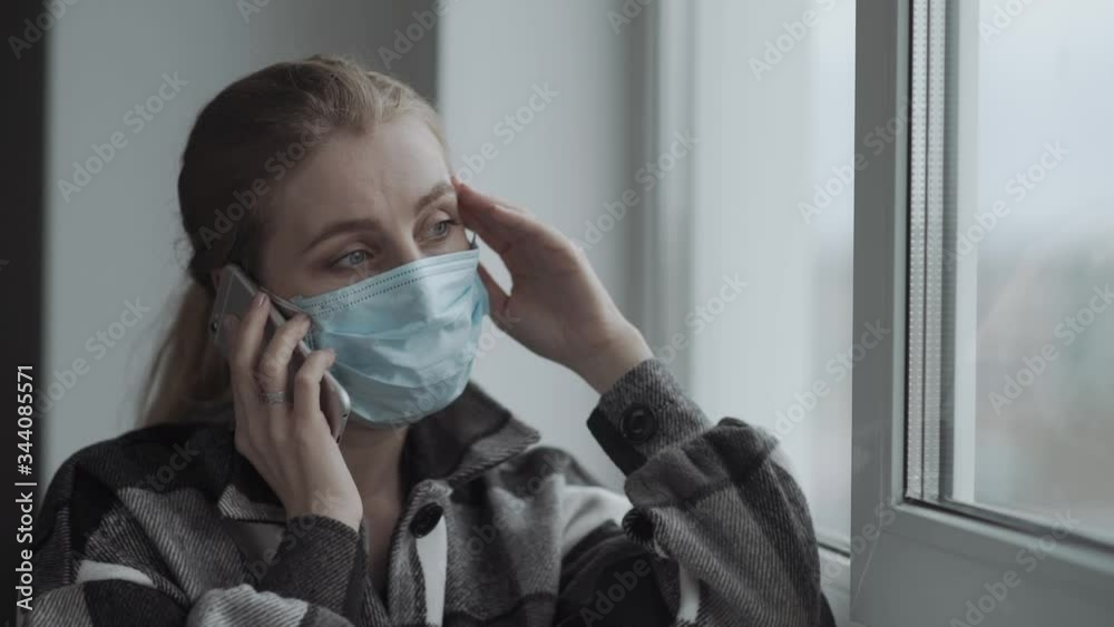 Close up portrait of woman near window speaking on phone. She talking to phone and looking aside, posing isolated over window. Coronavirus, Covid-19, healthcare concept. Copy space. Close up portrait of woman near window speaking on phone. She talking to phone and looking aside, posing isolated over window. Coronavirus, Covid-19, healthcare concept. Copy space.