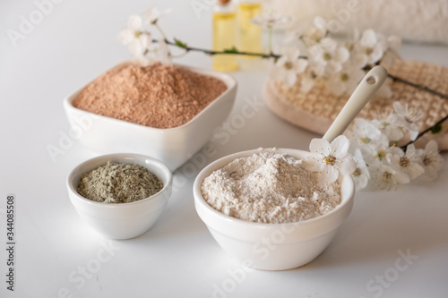 Ceramic bowl with red clay powder, ingredients for homemade facial and body mask or scrub and fresh sprig of flowering cherry . Spa and bodycare concept.