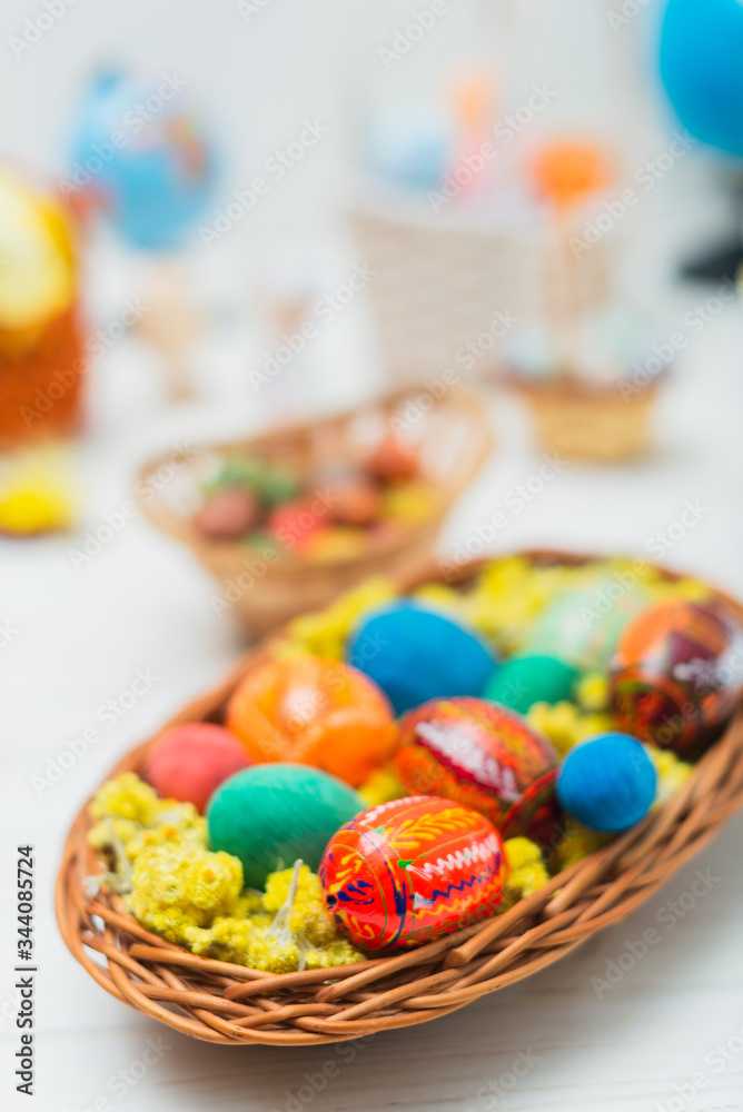 Fototapeta premium Multi-colored Easter eggs in a basket on a white wooden background