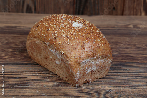 View of fresh bread sprinkled with sesame seeds. A freshly baked molded, golden loaf on a wooden, brown, rustic table. In the background brown boards.