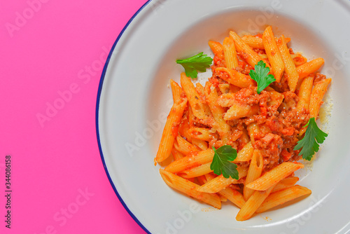 Plate of penne pasta with tomato sauce served in a white plate over bright pink background. Copy space banner.