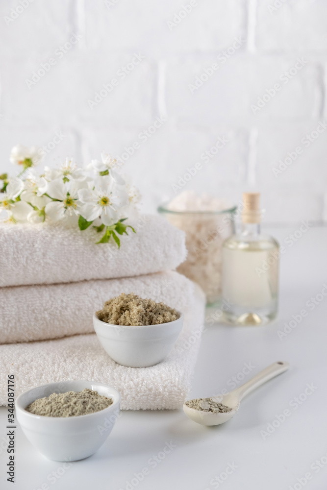 Set of different cosmetic clay mud powders on white background. Ingredients for homemade facial and body mask or scrub and fresh sprig of flowering cherry . Spa and bodycare concept.