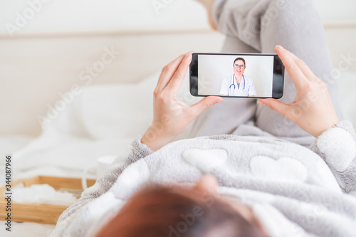 A woman is quarantined at home and is conducting a video conference with a virologist. The patient lies on the bed with a phone in her hands. Call from the doctor.