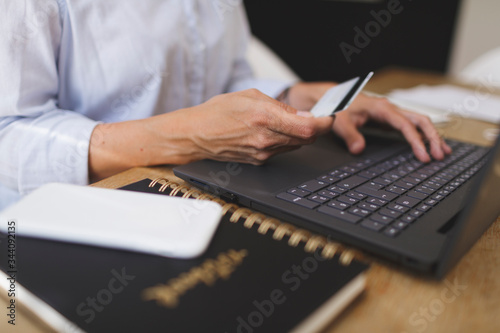 beautiful young business woman doing home online shopping with her laptop computer and credit card on the kitchen table during the corona crisis