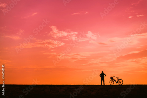 The silhouette of a cyclist against the background of the orange dawn sky.