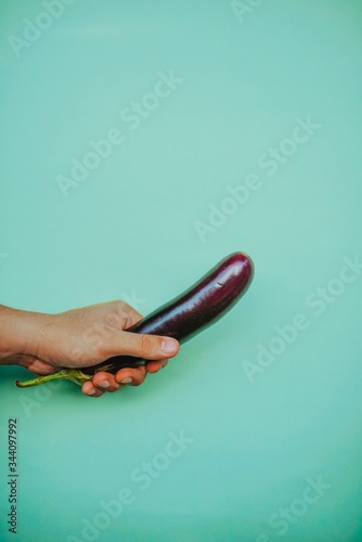 Hand firmly gripping eggplant with bright colorful background.