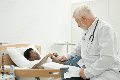Eldery doctor examinating belly of african patient.