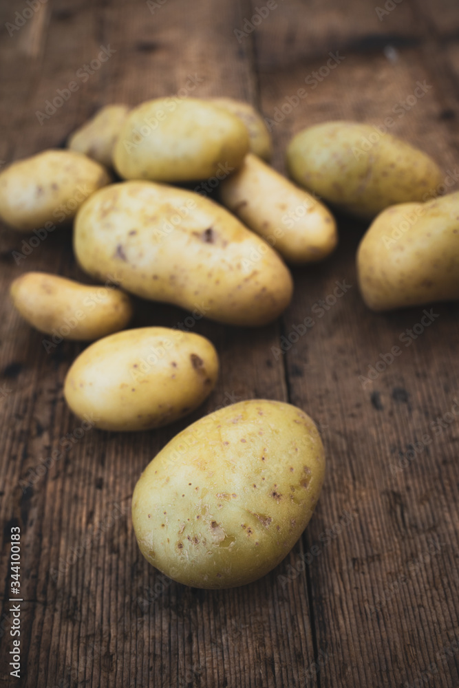 New potatoes, characteristic for their thin skin, are harvested when the ripening is not complete. In the photo potatoes on wooden table New potatoes, characteristic for their thin skin, are harvested when the ripening is not complete. In the photo potatoes on wooden table