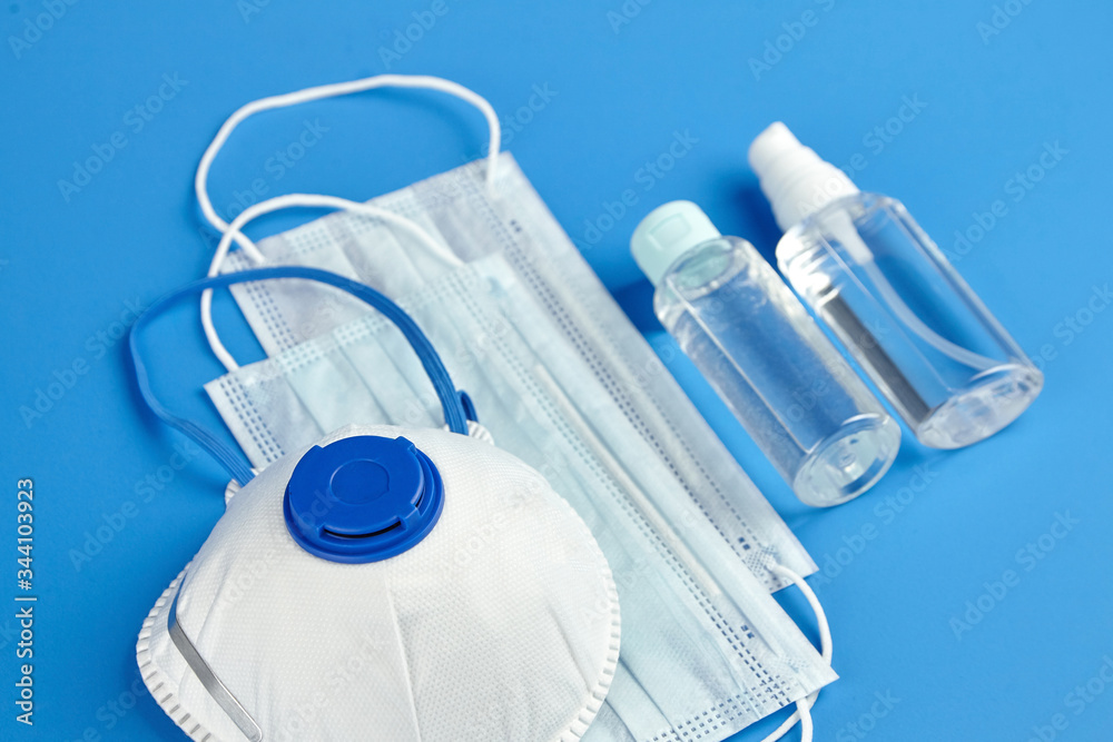 Respirator n95, FFP2, bottles of antibacterial hand sanitizer (alcohol antiseptic gel) and surgical masks on blue background Respirator n95, FFP2, bottles of antibacterial hand sanitizer (alcohol antiseptic gel) and surgical masks on blue background