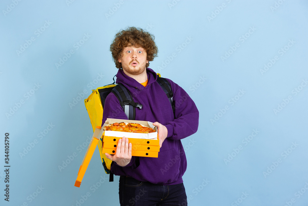 Shocked opening pizza boxes. Emotions of caucasian deliveryman isolated on blue background. Contacless delivery service during quarantine. Man delivers food during isolation. Safety. Hurrying up. Shocked opening pizza boxes. Emotions of caucasian deliveryman isolated on blue background. Contacless delivery service during quarantine. Man delivers food during isolation. Safety. Hurrying up.