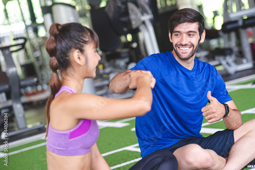 Caucasian man are punching hand and thumb up with his Asian woman friend in the gym after exercise cardio muscle training with smile and fresh face. Healthy care, body muscle builder concept.