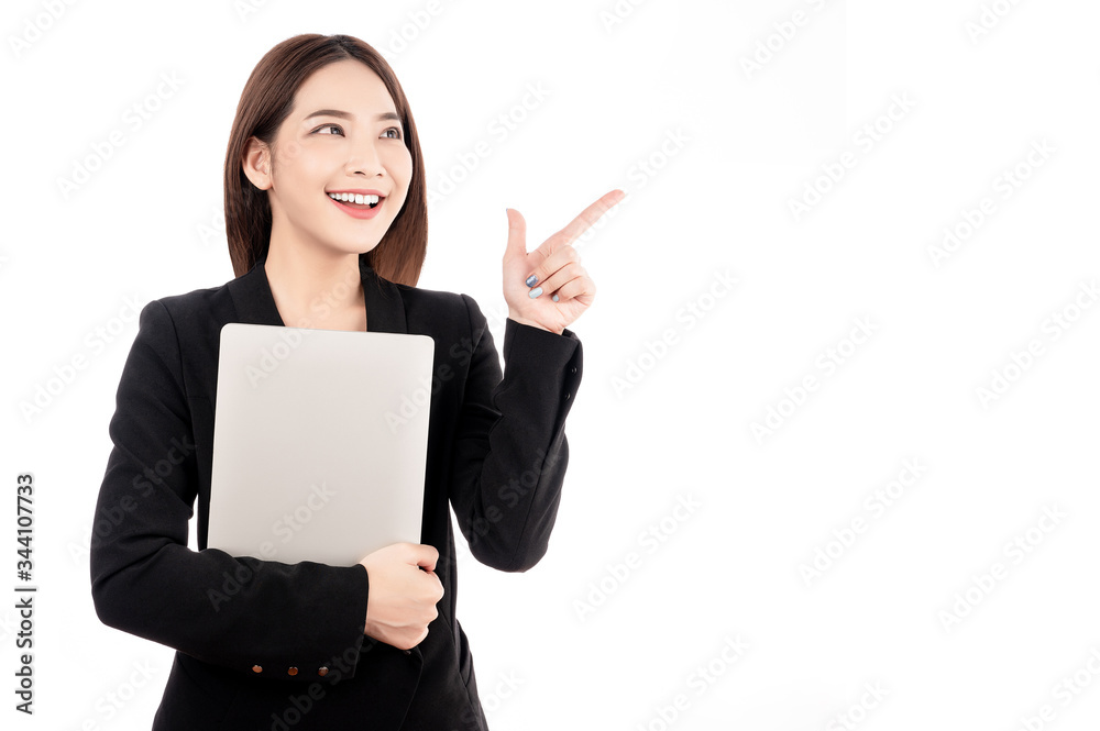 Asian businesswoman with black suit holding a laptop and pointing to present copy space with big smile beaming face in white isolated background. Asian businesswoman with black suit holding a laptop and pointing to present copy space with big smile beaming face in white isolated background.