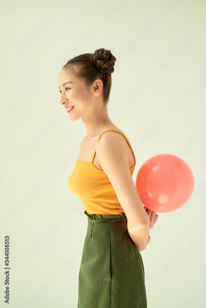 Adorable Asian girl holding a pink balloon while standing isolated on light background. Adorable Asian girl holding a pink balloon while standing isolated on light background.