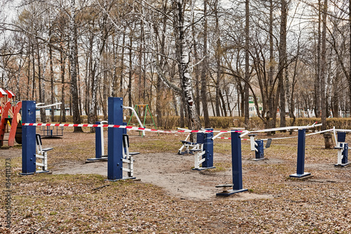 Fenced playground. Children's educational equipment is wrapped with warning tape in white and red. Nobody here. Forbidden located in public areas.