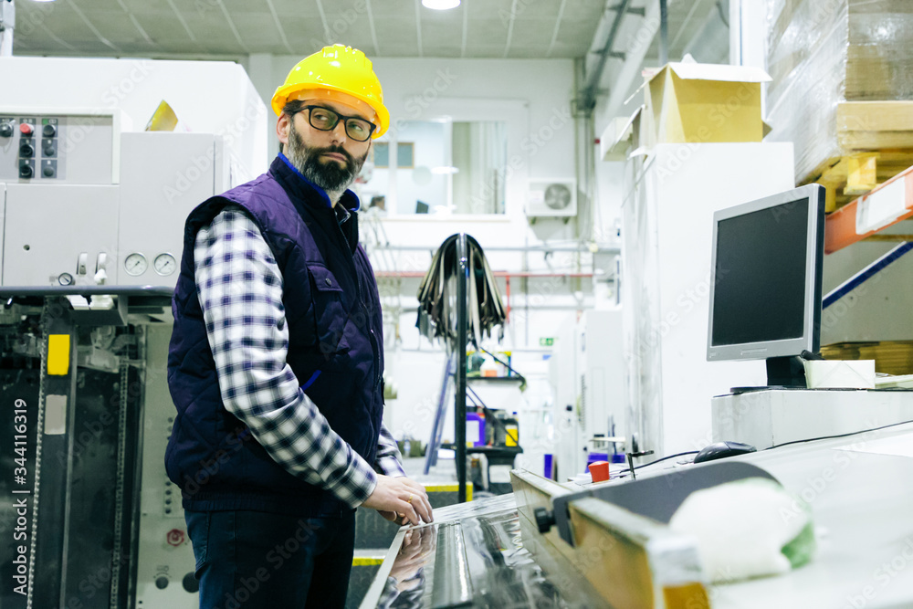 Pensive male factory worker operating milling machine. Bearded middle aged man in hardhat working at plant. Production process operator concept Pensive male factory worker operating milling machine. Bearded middle aged man in hardhat working at plant. Production process operator concept