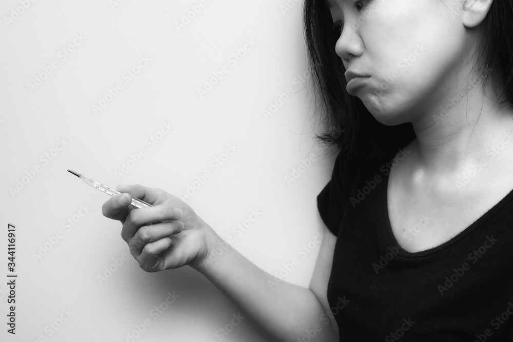 Asian woman looking at clinical thermometer on her hand for checking temperature. Black and white tone. Diagnosis and test COVID-19. Asian woman looking at clinical thermometer on her hand for checking temperature. Black and white tone. Diagnosis and test COVID-19.