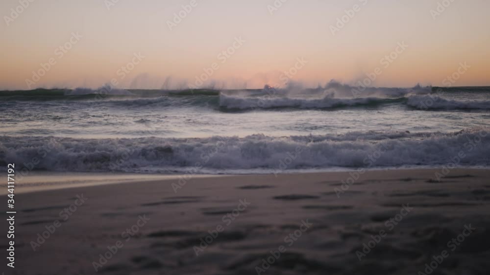 Sun setting on ocean horizon as waves crash on an empty beach. Golden hour sunset. Footprints in the sand. Sun setting on ocean horizon as waves crash on an empty beach. Golden hour sunset. Footprints in the sand.
