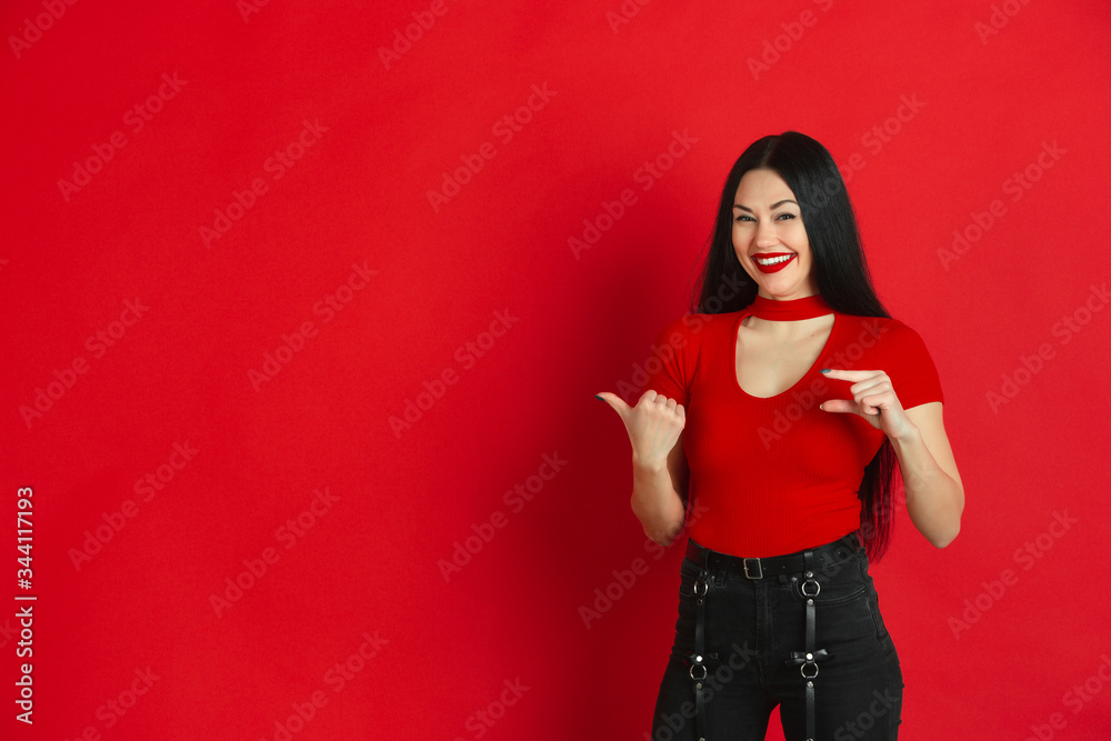Showing something little, laughting. Caucasian young woman's monochrome portrait isolated on red studio background. Beautiful brunette model. Concept of human emotions, facial expression, sales, ad. Showing something little, laughting. Caucasian young woman's monochrome portrait isolated on red studio background. Beautiful brunette model. Concept of human emotions, facial expression, sales, ad.
