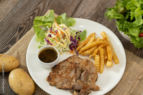 The plate of grilled pork steak with side dish french fries and salad. Decorated with potatoes on the wooden table