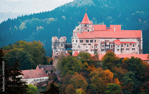 Medieval castle of Pernstein on a hill in the autumn forest. South Moravian region. Czech Republic. Red tiled roof. Historical building. Heritage of gothic. Beautiful shot of sightseeing.