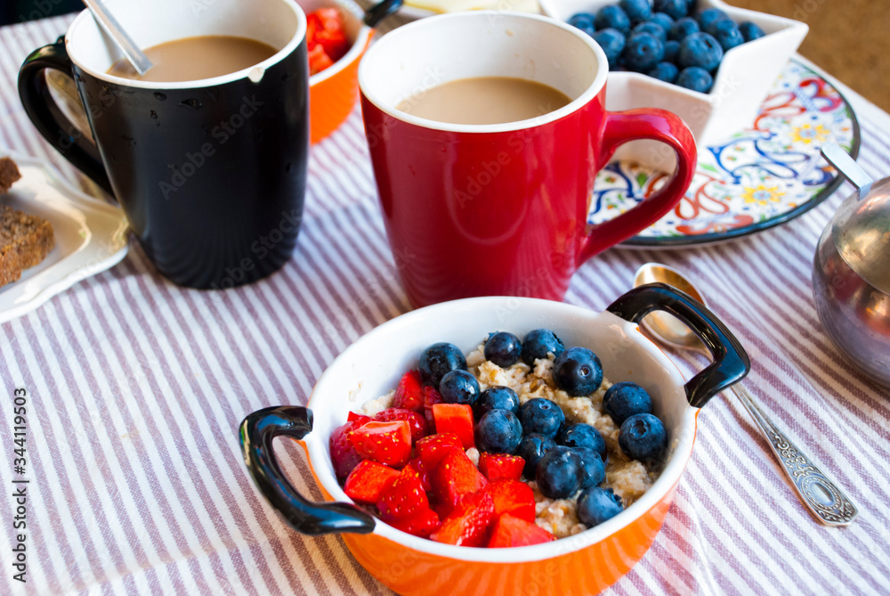 Breakfast for two person with coffee in big cup and bowl of oatmeal with berries. Breakfast for two person with coffee in big cup and bowl of oatmeal with berries.