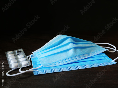 Disposable medical 3ply face mask with earloops and a blister of pills over dark background photo